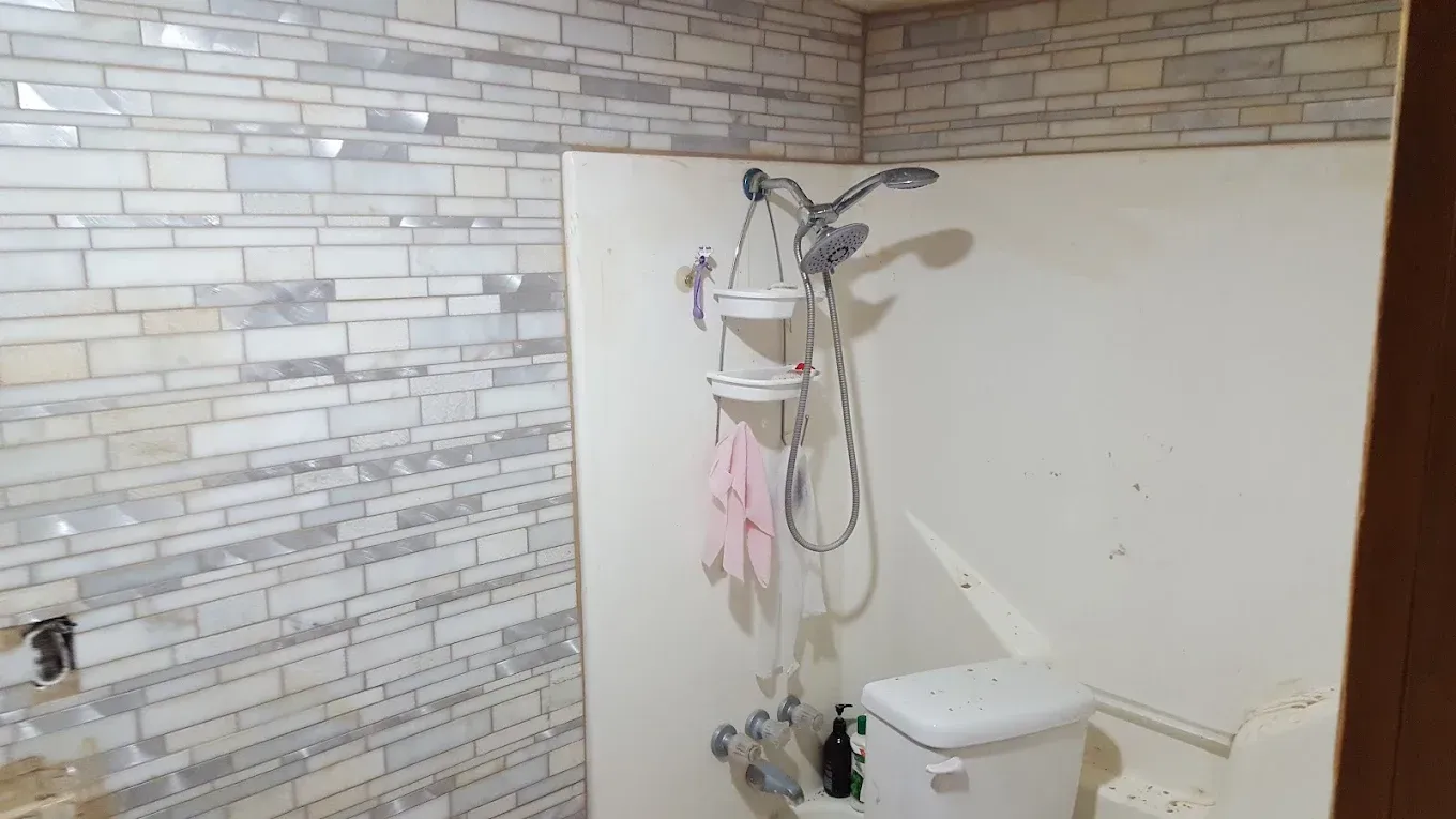 Shower area with handheld showerhead, white toilet, and stone-patterned wall tiles