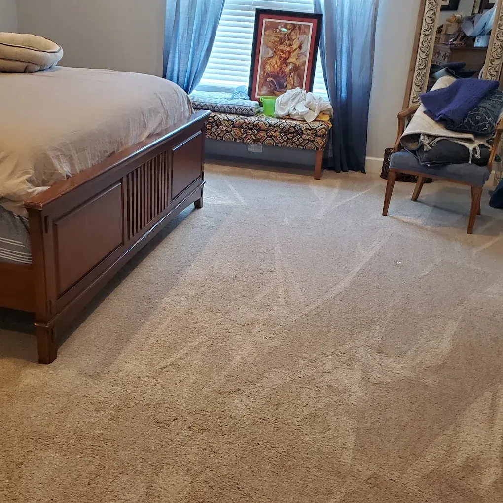 Bedroom with beige carpet, wooden bed, window seat, and chair near blue curtains