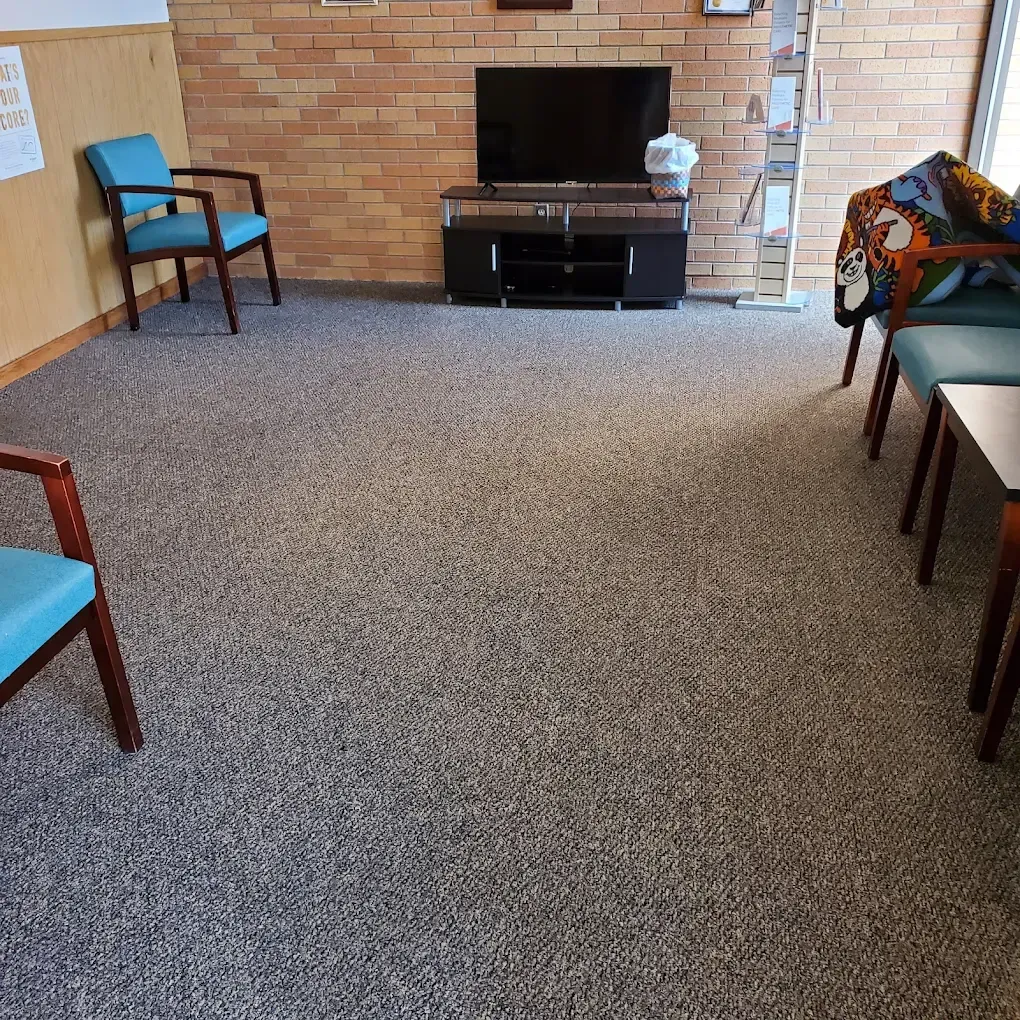 Living room with brick wall, TV stand, and scattered chairs on a carpeted floor