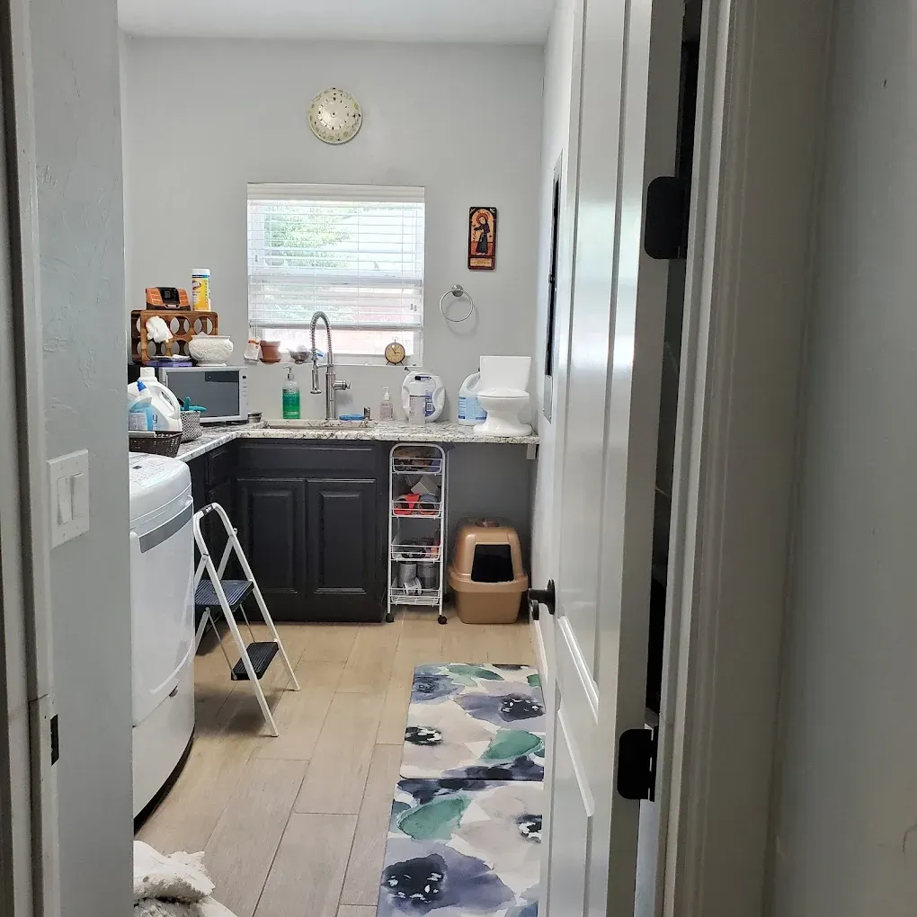 Kitchen with dark cabinets, white appliances, sink under a window, and a narrow rug on the floor.