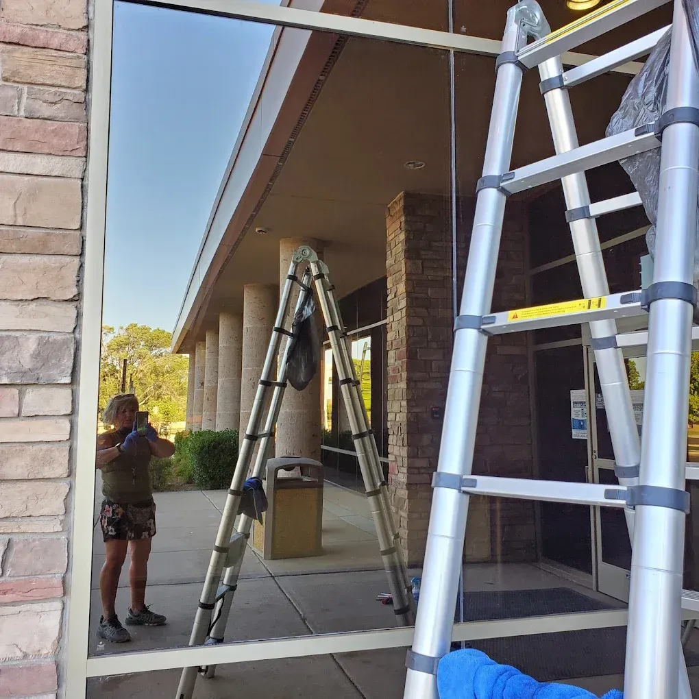 Person on a ladder beside a building entrance, with multiple ladders set up under a covered walkway.