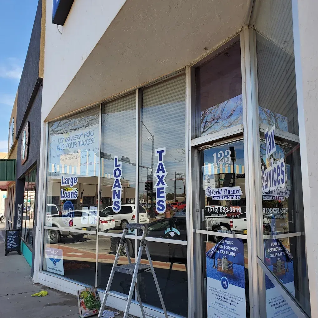 Storefront windows with signs for loans and taxes, reflecting cars on a sunny street.