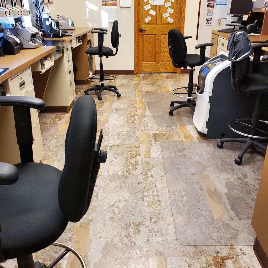 Empty office with desks, black chairs, and a wood door along a narrow carpeted aisle.