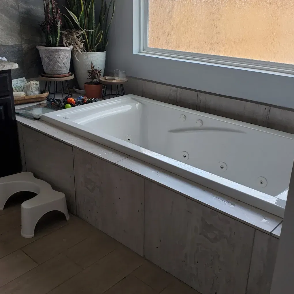 Modern bathroom with a large white built-in bathtub, gray paneling, and potted plants by a window