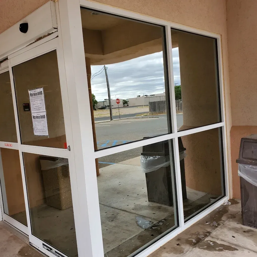 Empty storefront entrance with glass doors and windows, showing a trash can and sidewalk outside