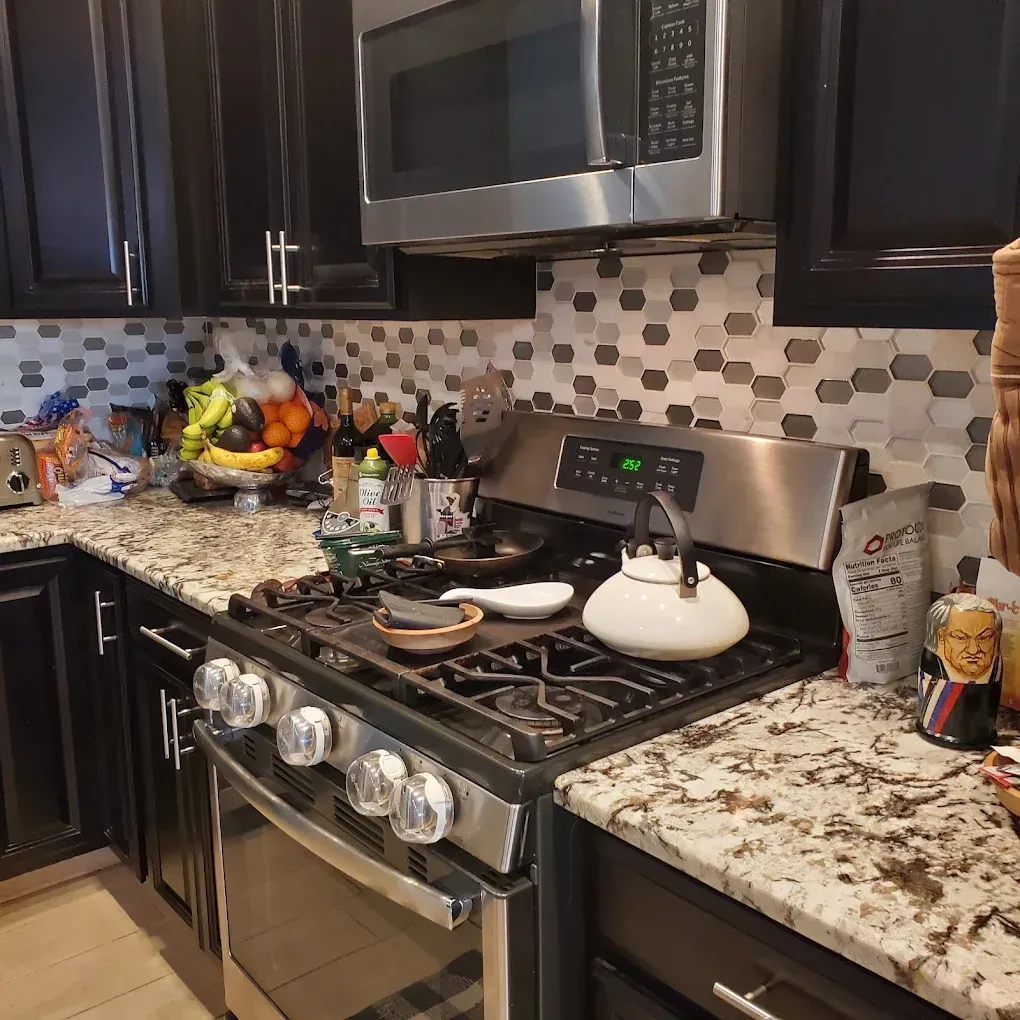 Modern kitchen with black cabinets, granite countertops, stainless stove, microwave, and checkered backsplash