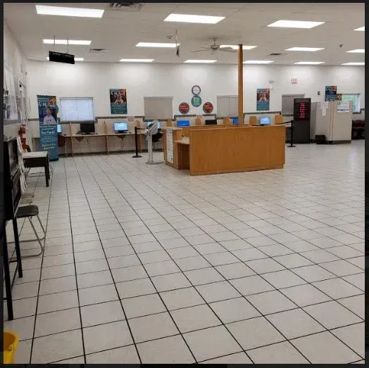 Empty public office lobby with tiled floor, service counters, and computer stations under fluorescent lights