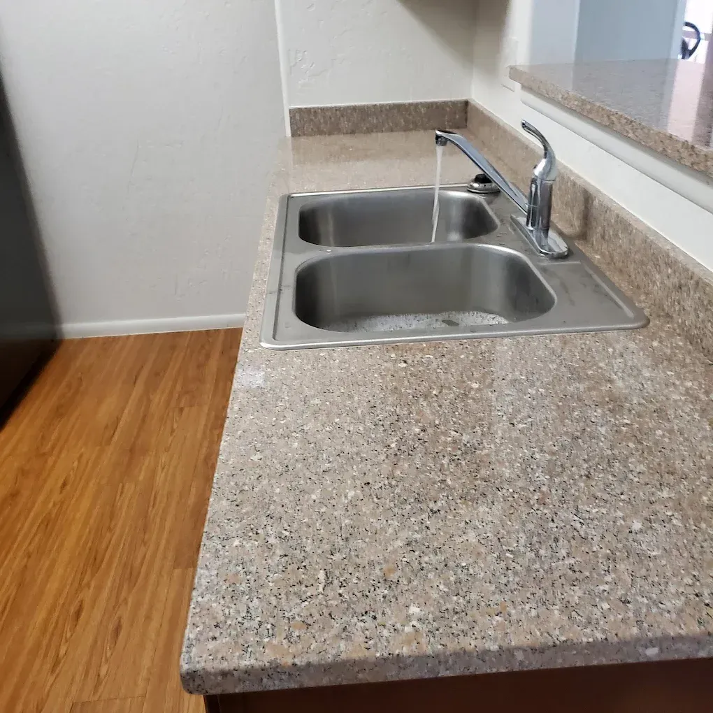 Kitchen countertop with double stainless steel sink and chrome faucet beside a wall.