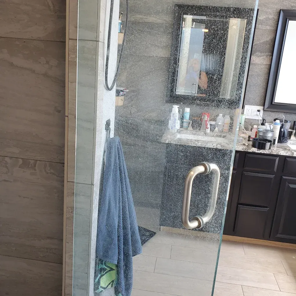 Bathroom with glass shower door, blue towel, and dark vanity with sink and mirror.
