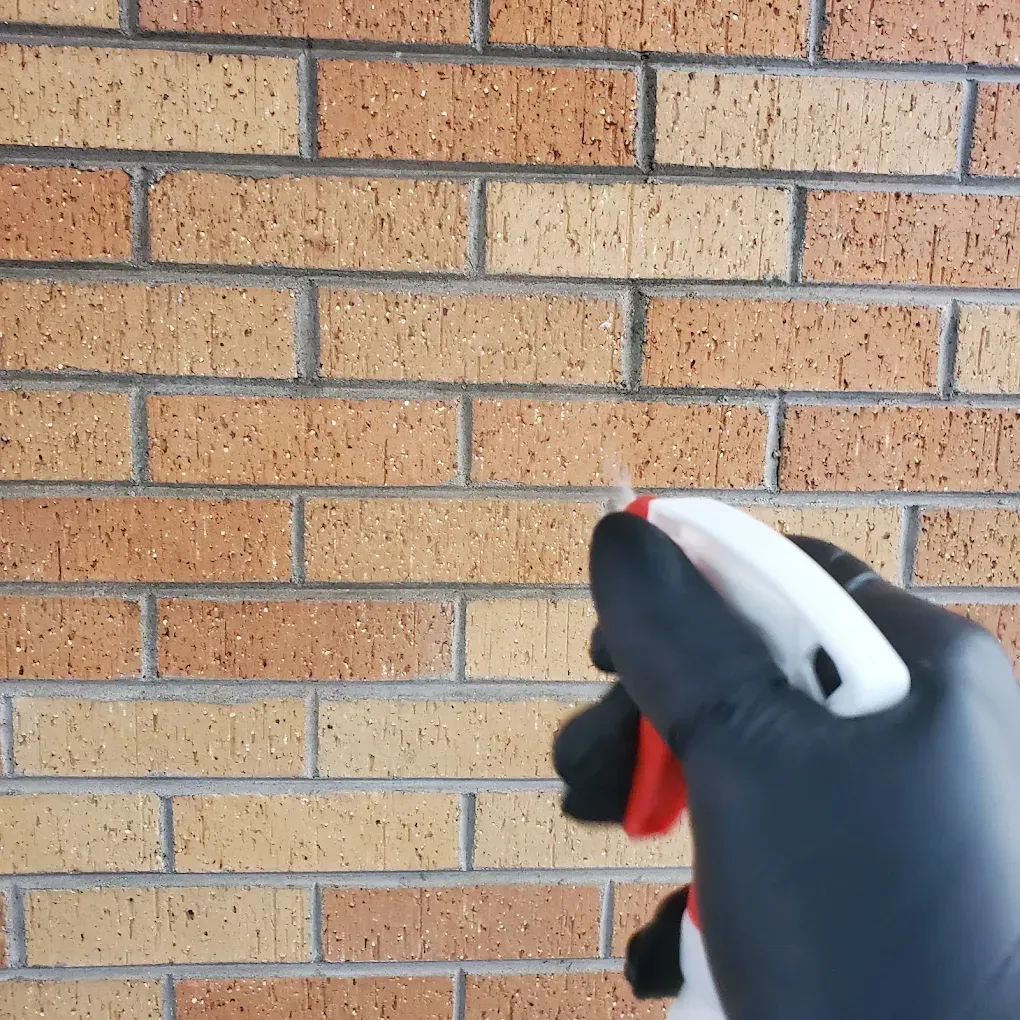 Gloved hand spraying cleaner on a tan brick wall