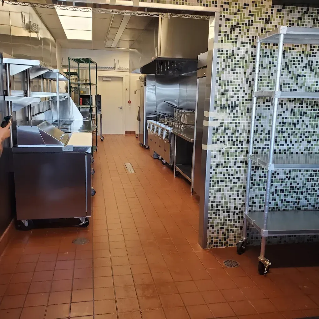 Commercial kitchen with stainless steel prep tables, tiled floor, and mosaic-tile wall accents