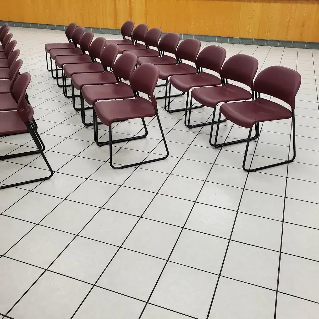 Rows of maroon chairs in an empty meeting room with tiled floor and wood-paneled wall