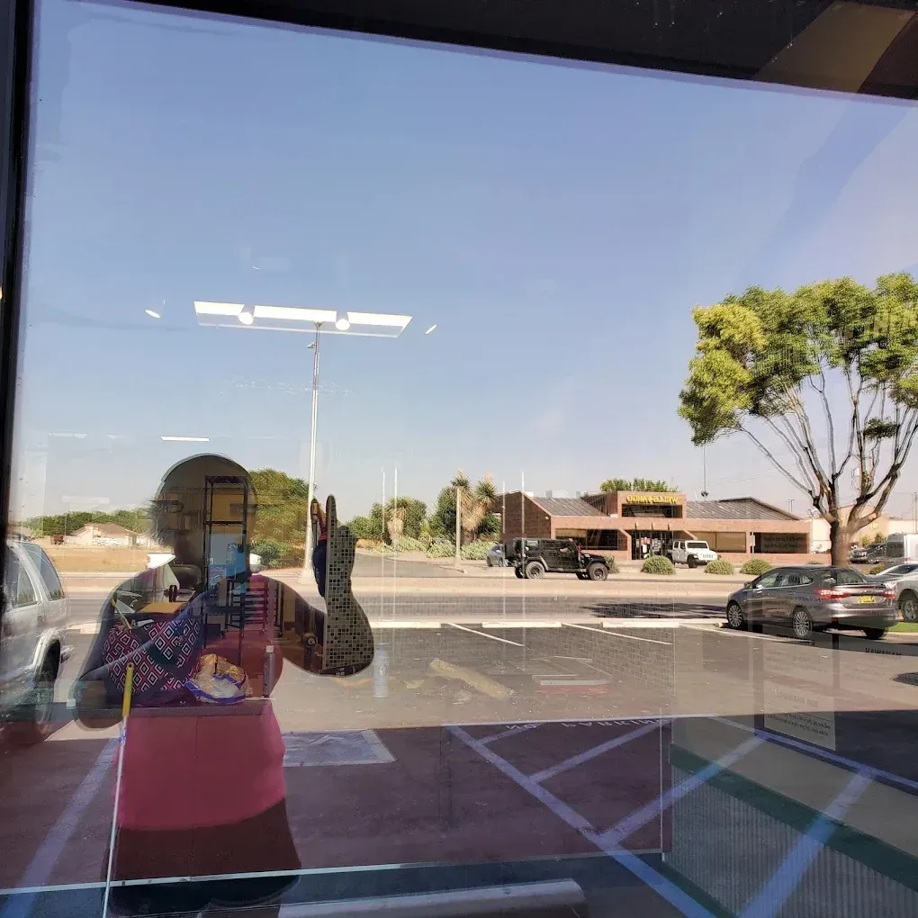 Person taking a mirror selfie inside a building, reflecting a sunny parking lot and street outside.