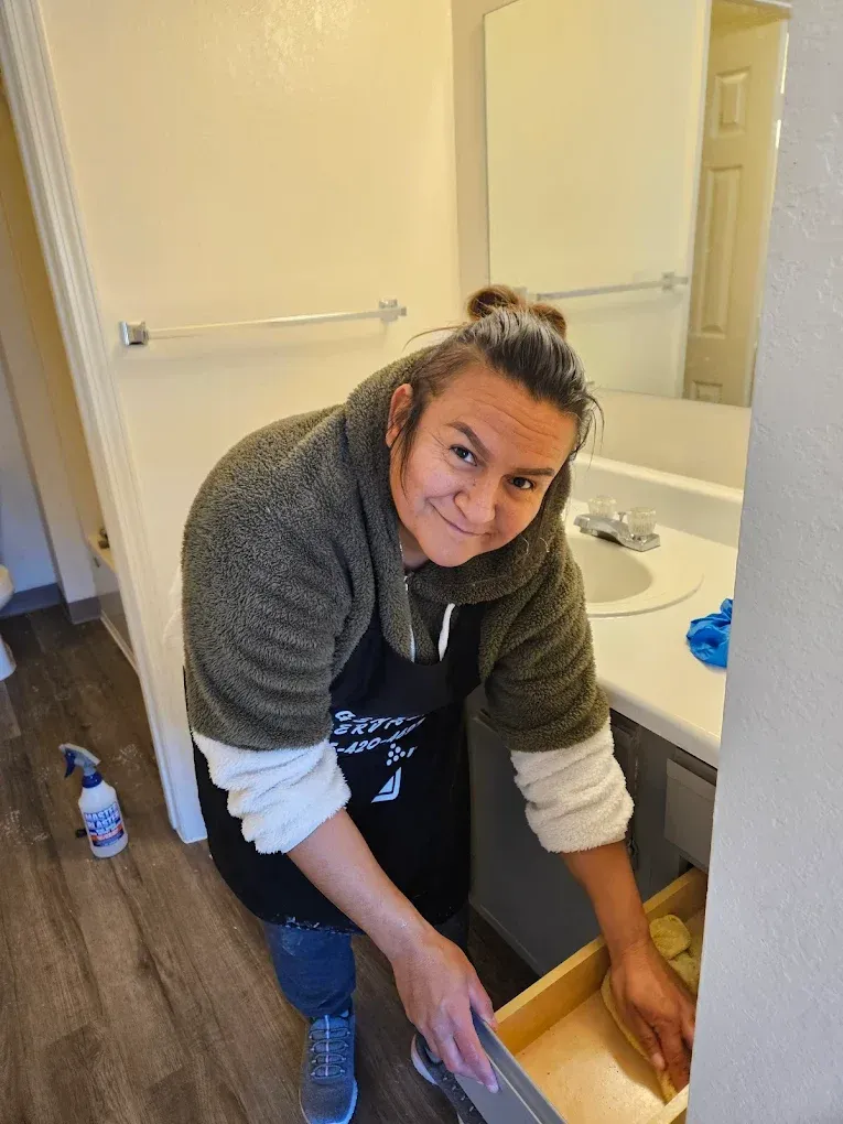Person kneeling in a bathroom, cleaning the floor beside a sink and mirror.