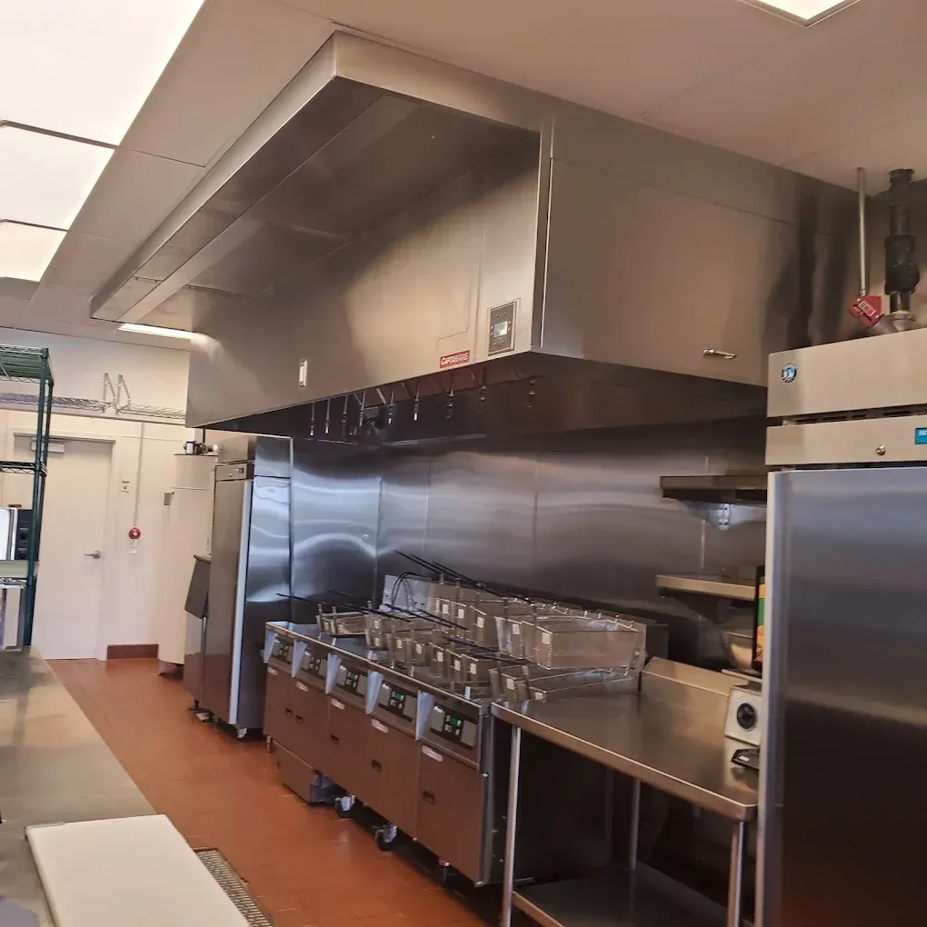 Commercial kitchen with stainless-steel appliances, counters, and trays under a large ventilation hood