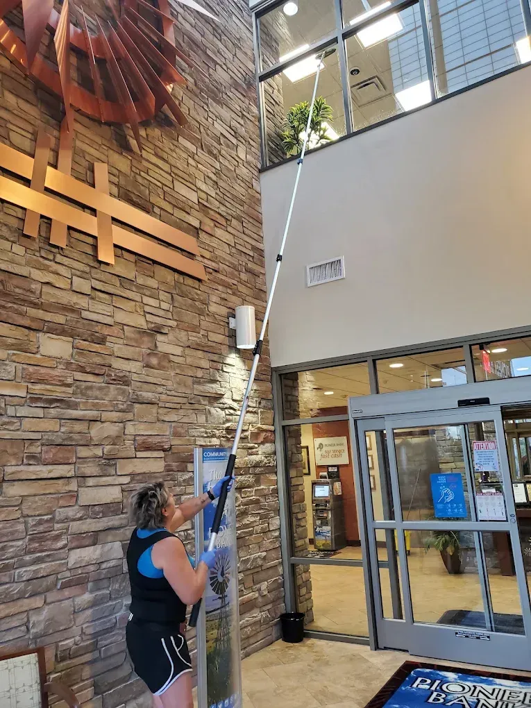 Person using a long pole to reach a high indoor ceiling in a lobby entrance
