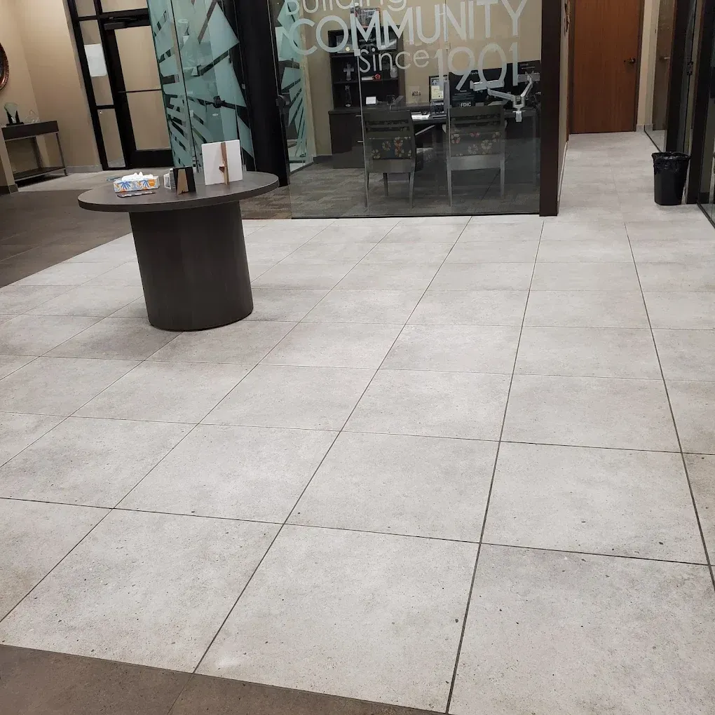 Indoor mall corridor with tiled floor, a round display table, and storefront glass doors in the background