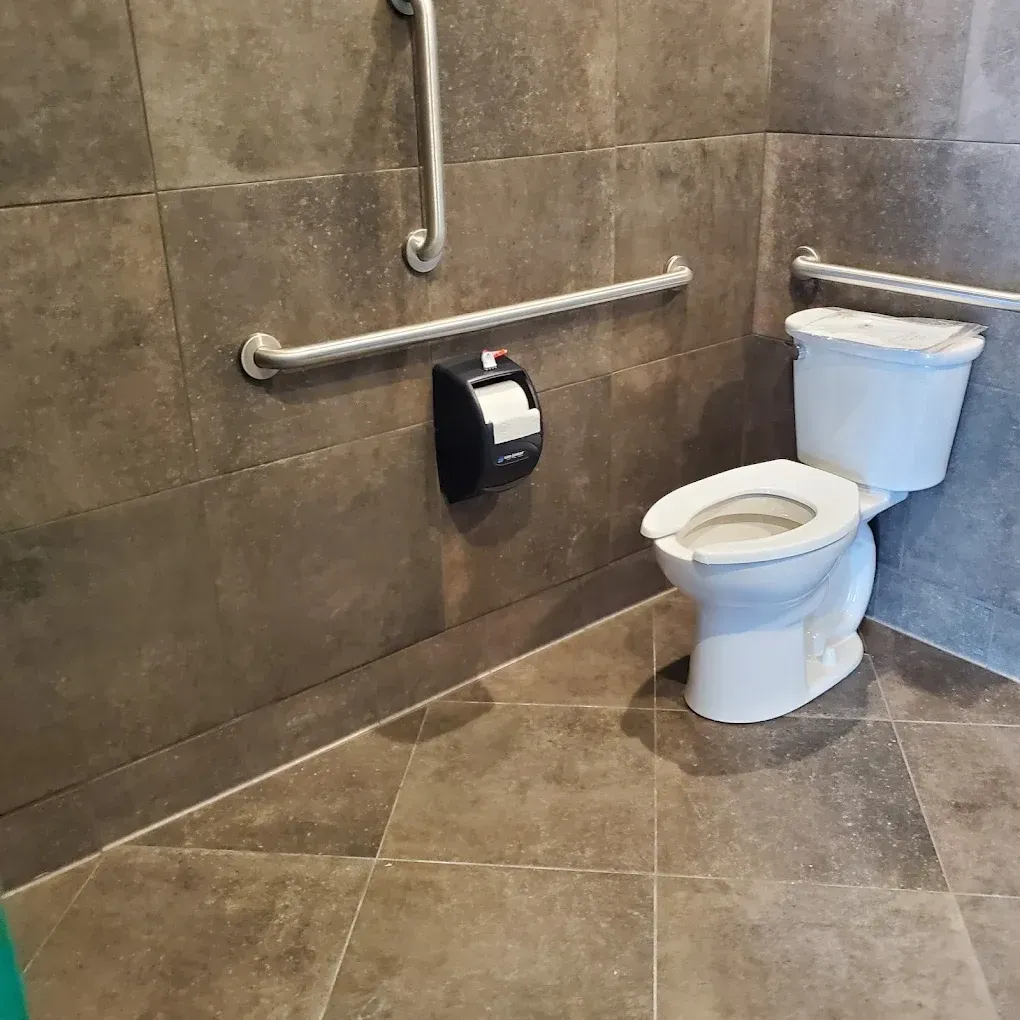 Accessible restroom with a toilet, toilet paper holder, and grab bars on tiled walls and floor