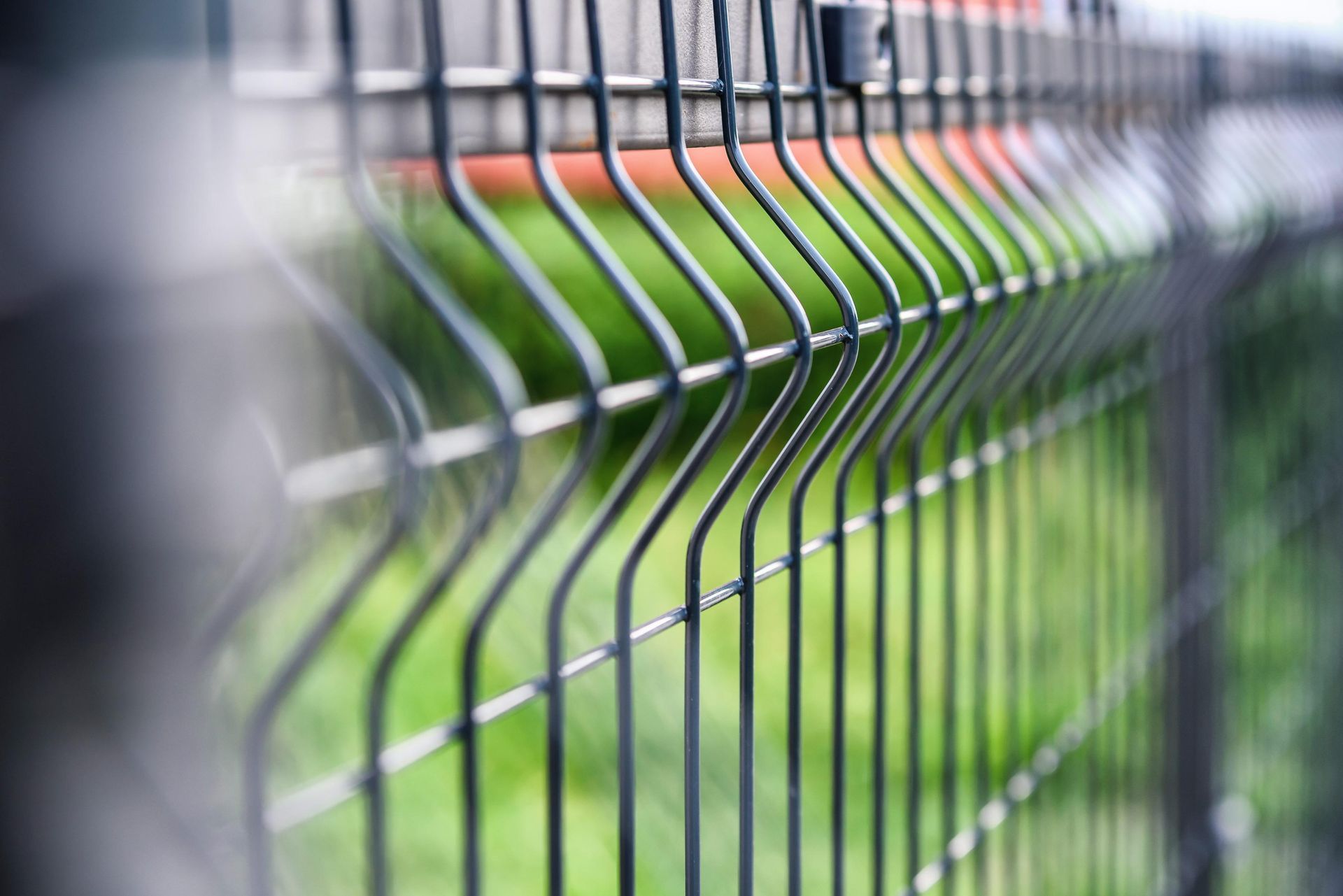 Metal wire fence in a curved pattern, green grass and out-of-focus background.