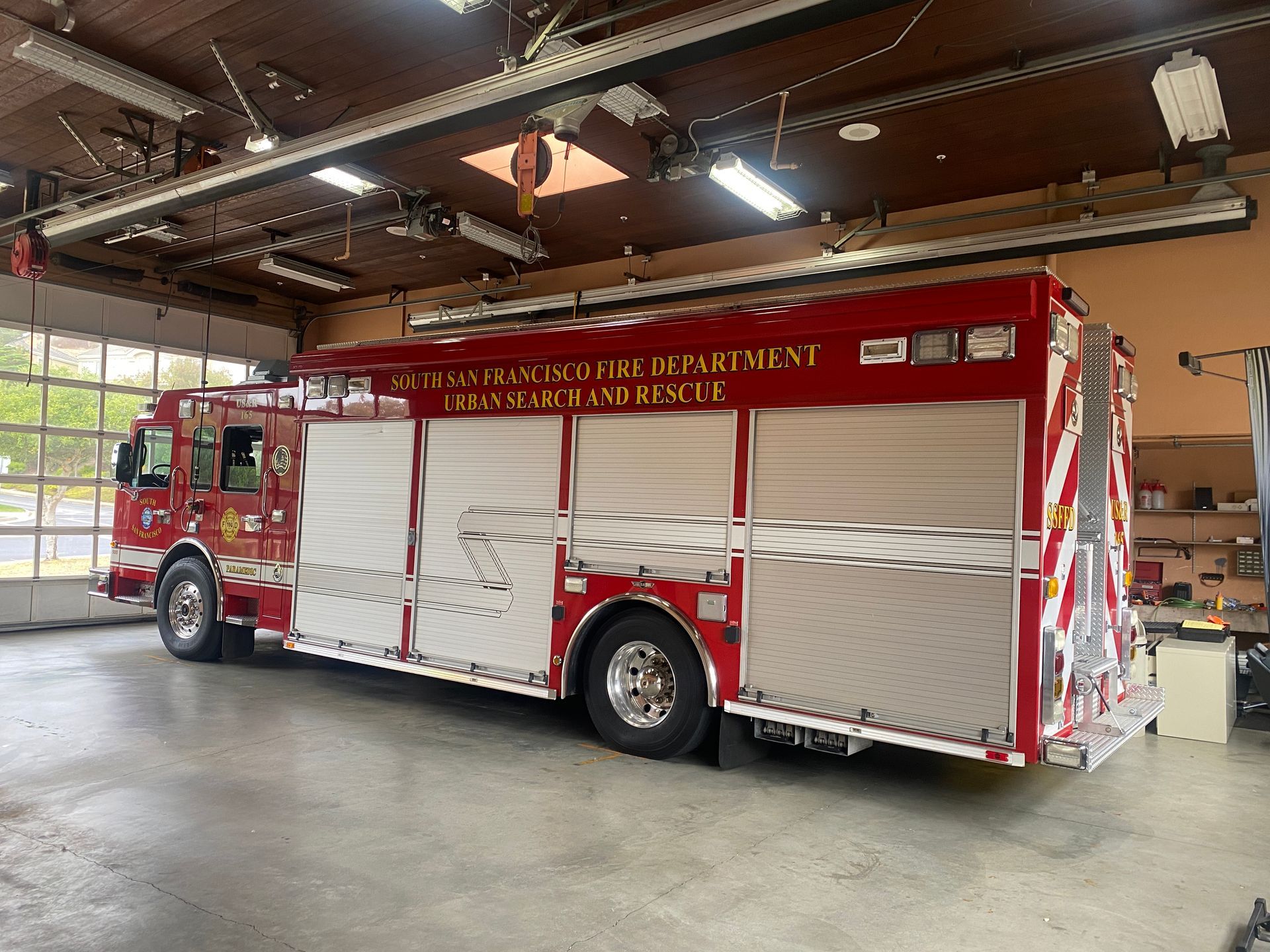 Red fire truck parked inside a garage, with silver compartments and lettering indicating the county.