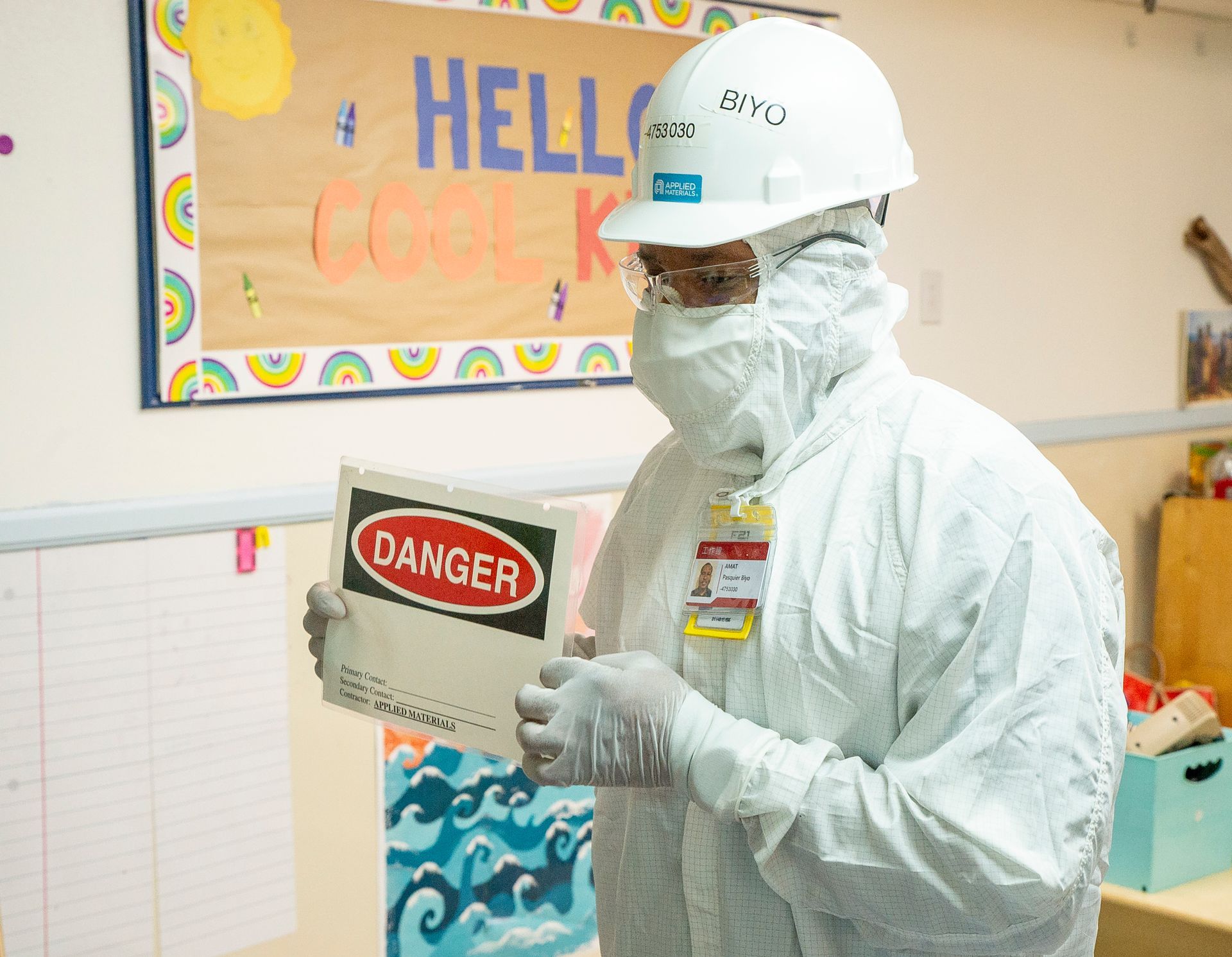Person in white safety gear holding a “DANGER” sign in a colorful indoor hallway.
