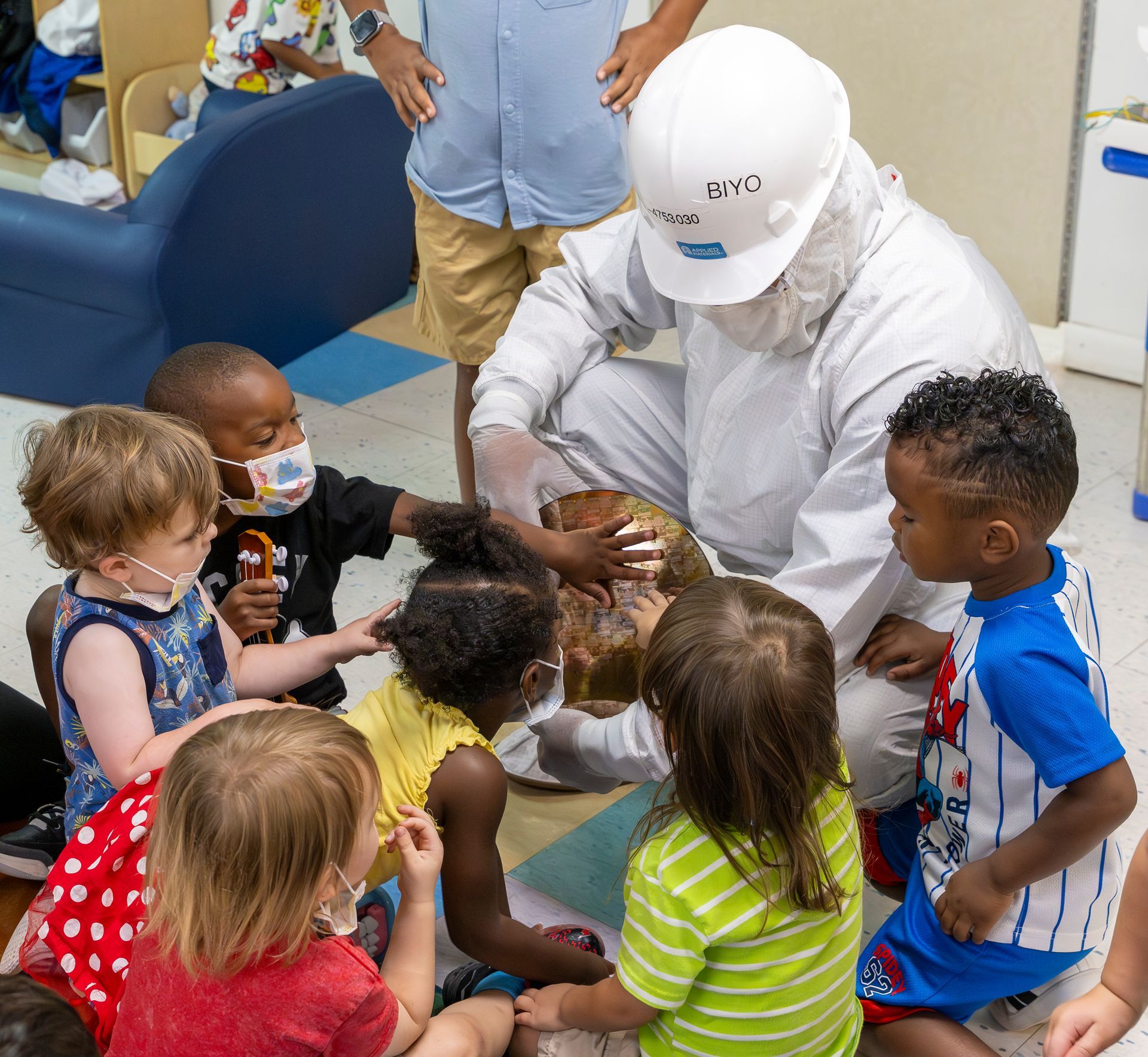 Healthcare worker kneels with young children in a playroom, engaging them around a small activity.