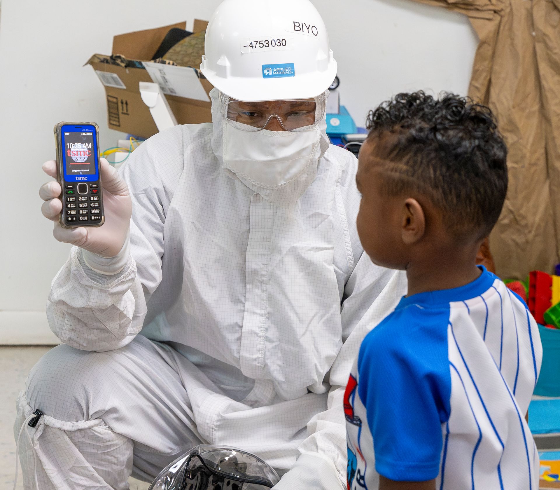 Healthcare worker in white protective suit showing a phone to a child in a clinic