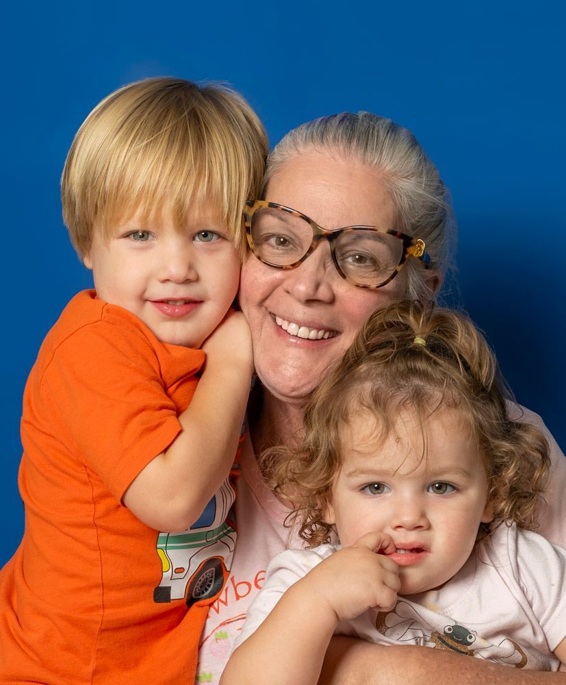 Three smiling people posing close together against a blue background, two children and one adult wearing glasses