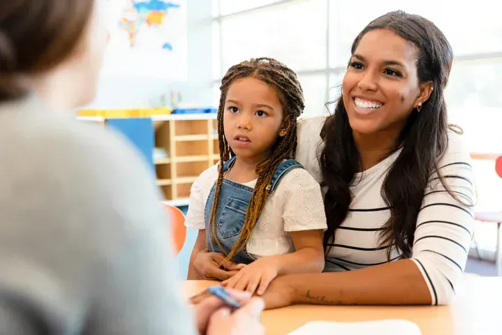 Woman smiling beside a child at a table in a bright classroom setting