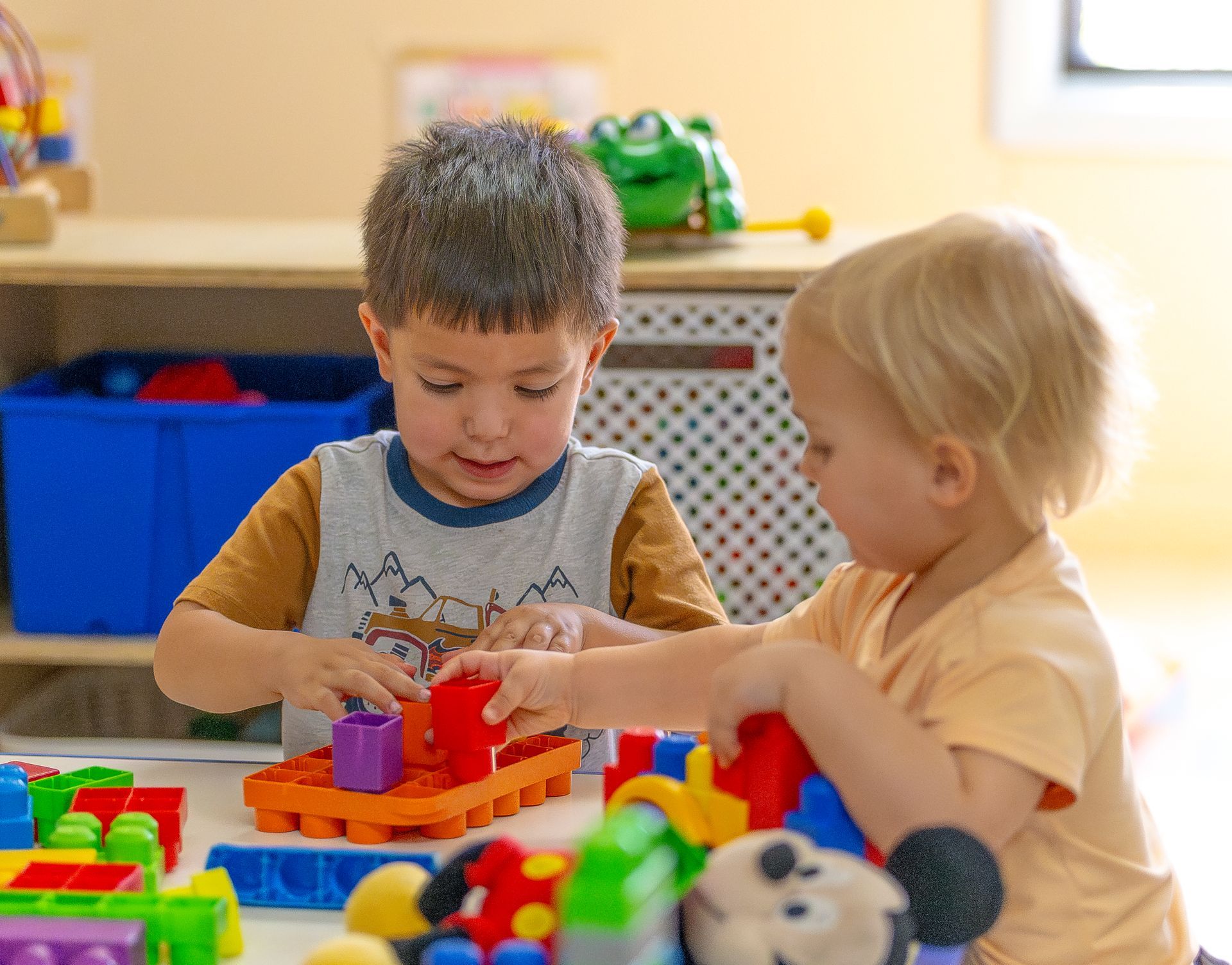 Two children play with colorful building blocks at a table in a bright classroom