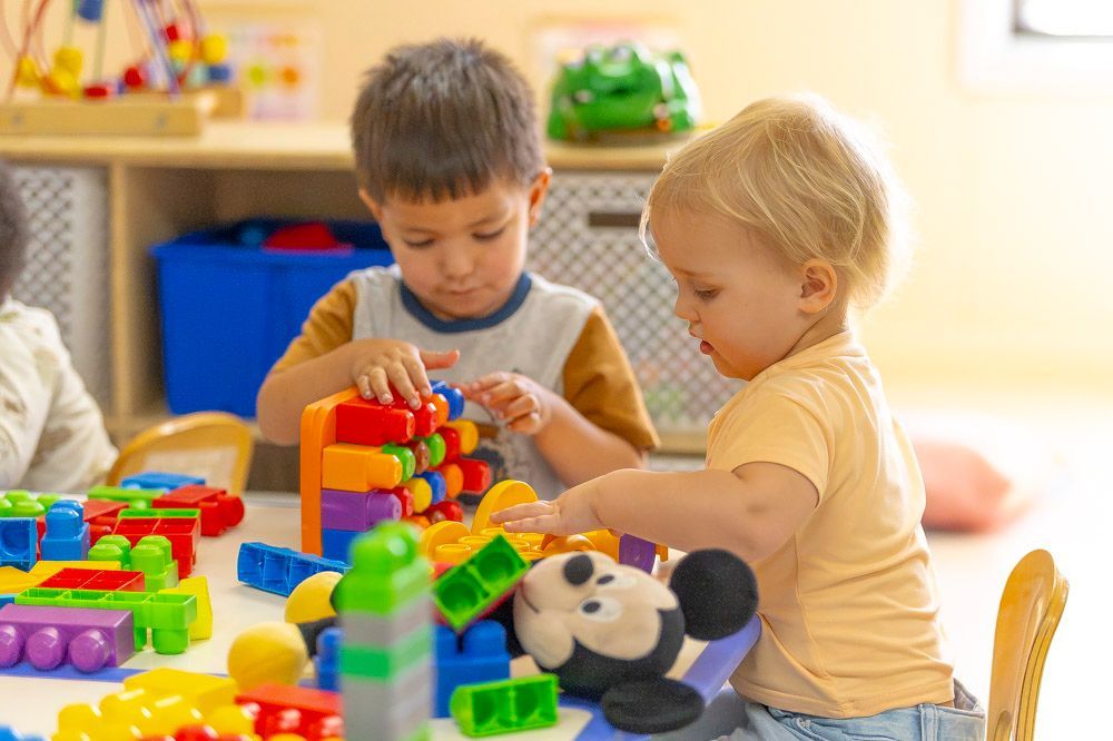 Two children playing with colorful building blocks on a floor, focused on stacking toys