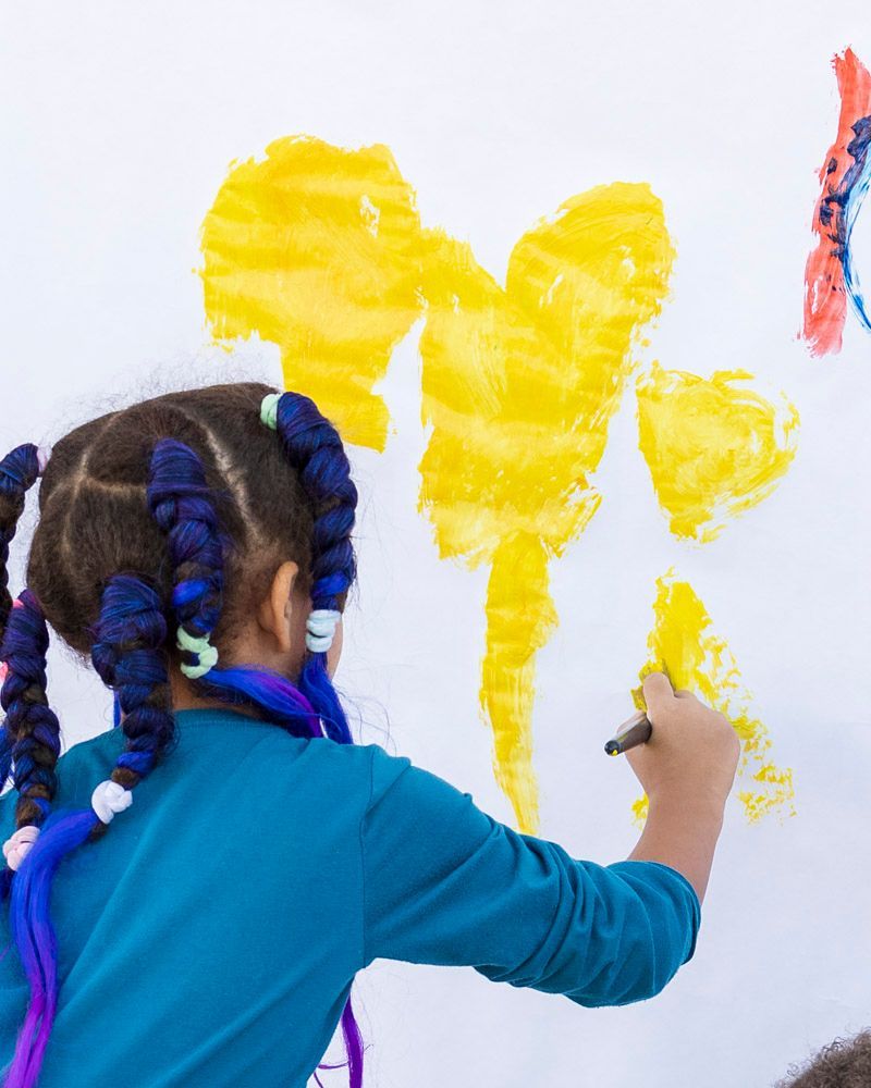 Child painting yellow shapes on a white wall with a brush
