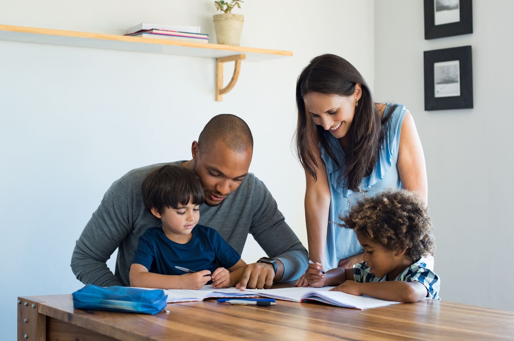 Adult helping two children do homework at a table in a bright room