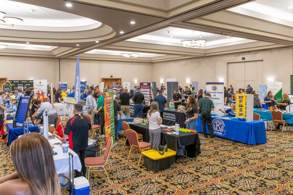 Crowded conference expo with vendor booths, blue tablecloths, and attendees browsing displays in a hotel ballroom