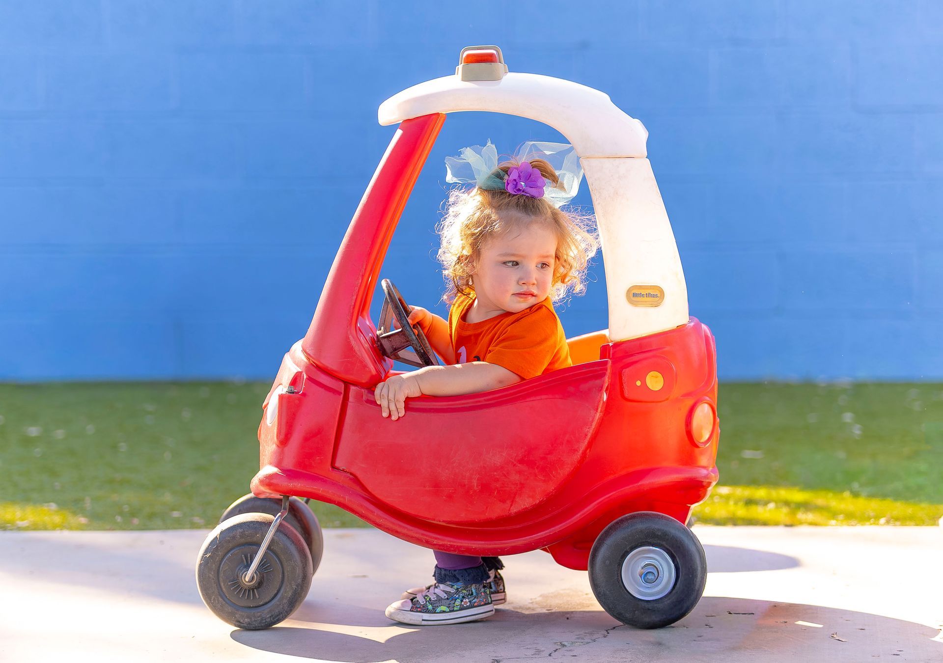 Child sitting in a red toy car outdoors on a sunny day
