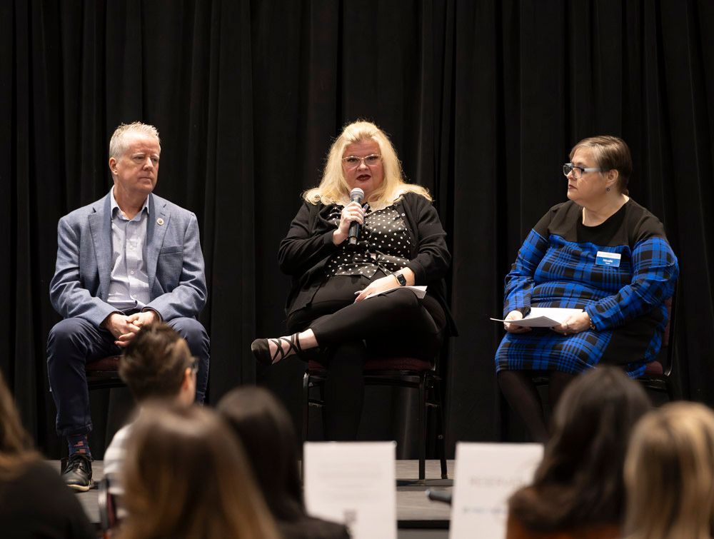 Three panelists seated on stage in front of an audience, speaking during a discussion event.