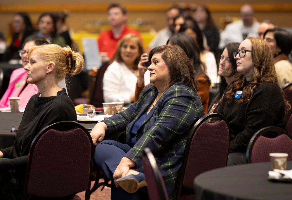 Audience members seated at round tables listening in a conference room