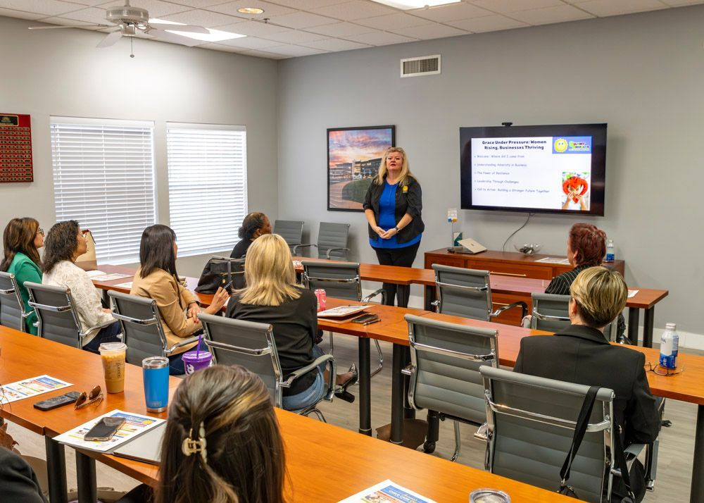 Classroom presentation with students seated at tables facing a presenter and wall-mounted screen.