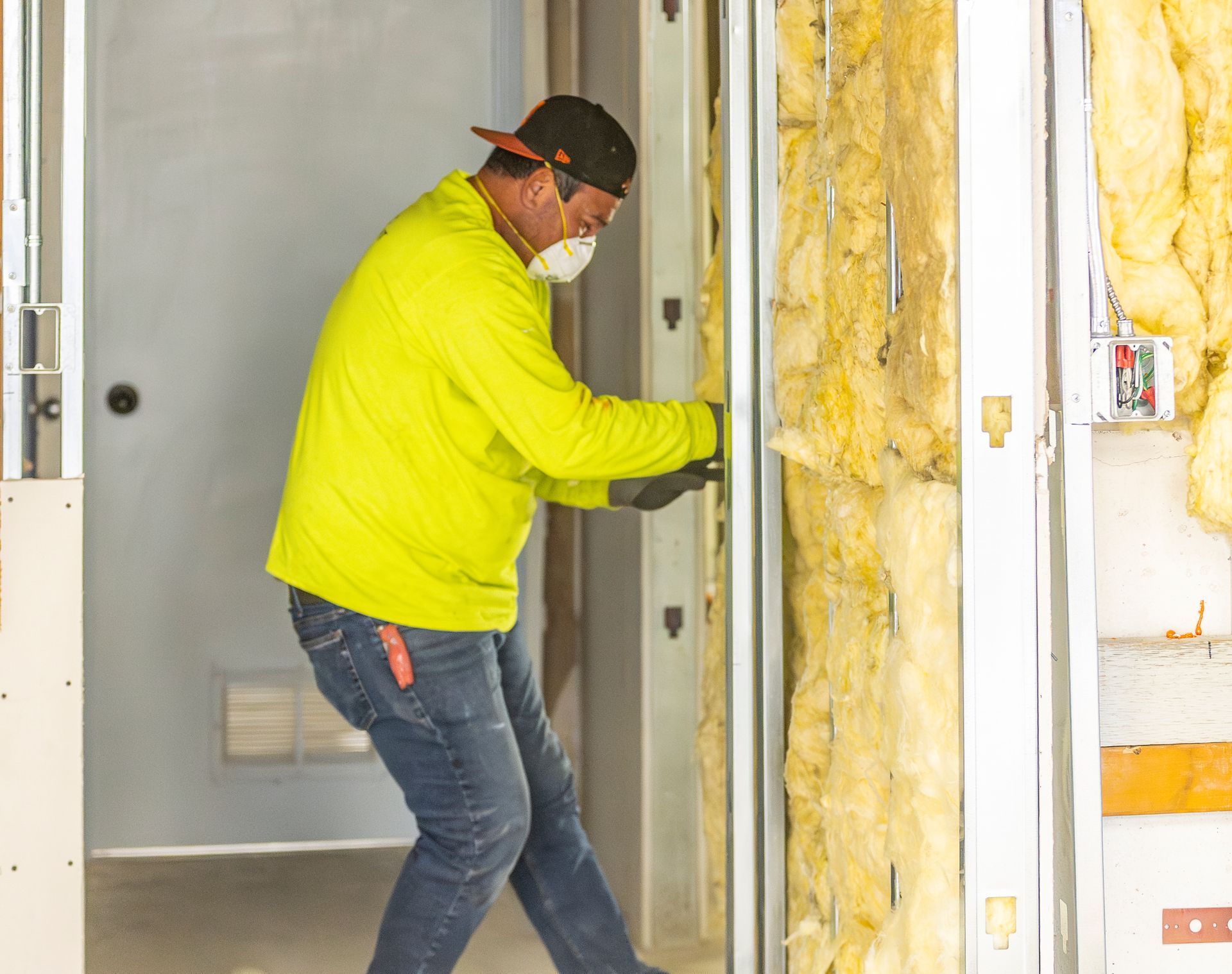 Worker in a neon yellow jacket insulating a wall inside a doorway.