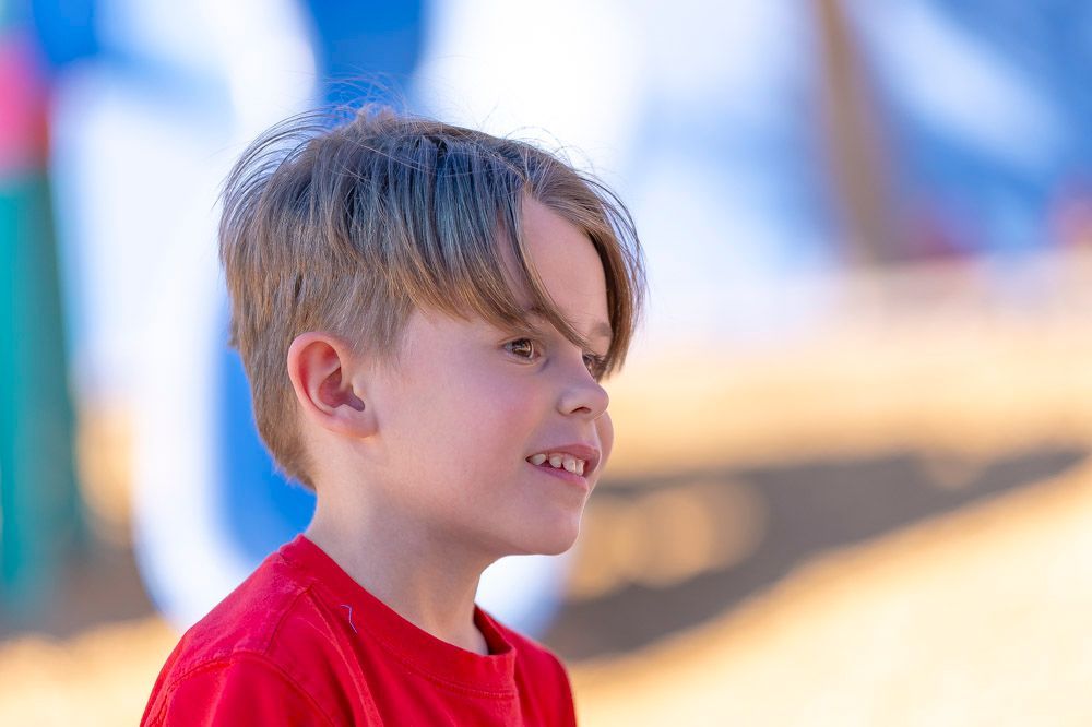 Child in a red shirt smiling in profile outdoors with a blurred blue and tan background