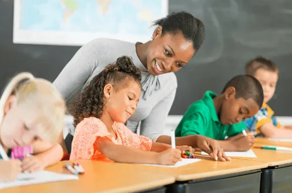 Teacher helping students write at desks in a classroom