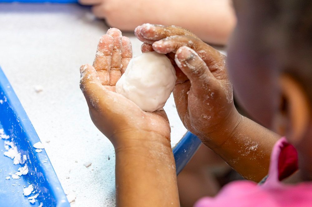 Child’s hands shaping white clay on a table, with a blue edge in the background