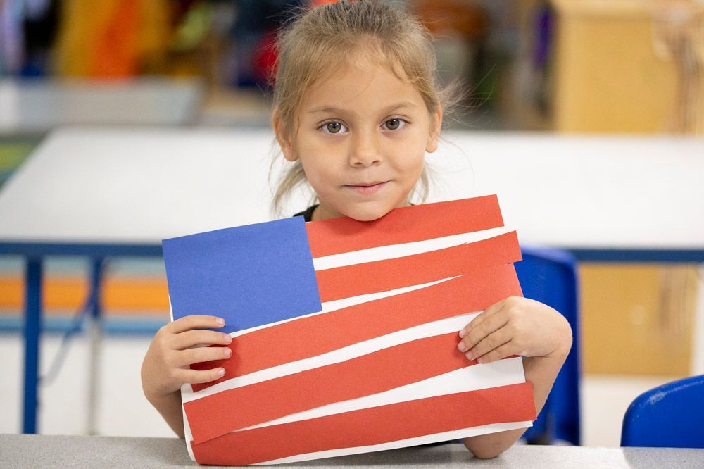 Child holding a small American flag craft with red and white stripes and a blue corner flag field