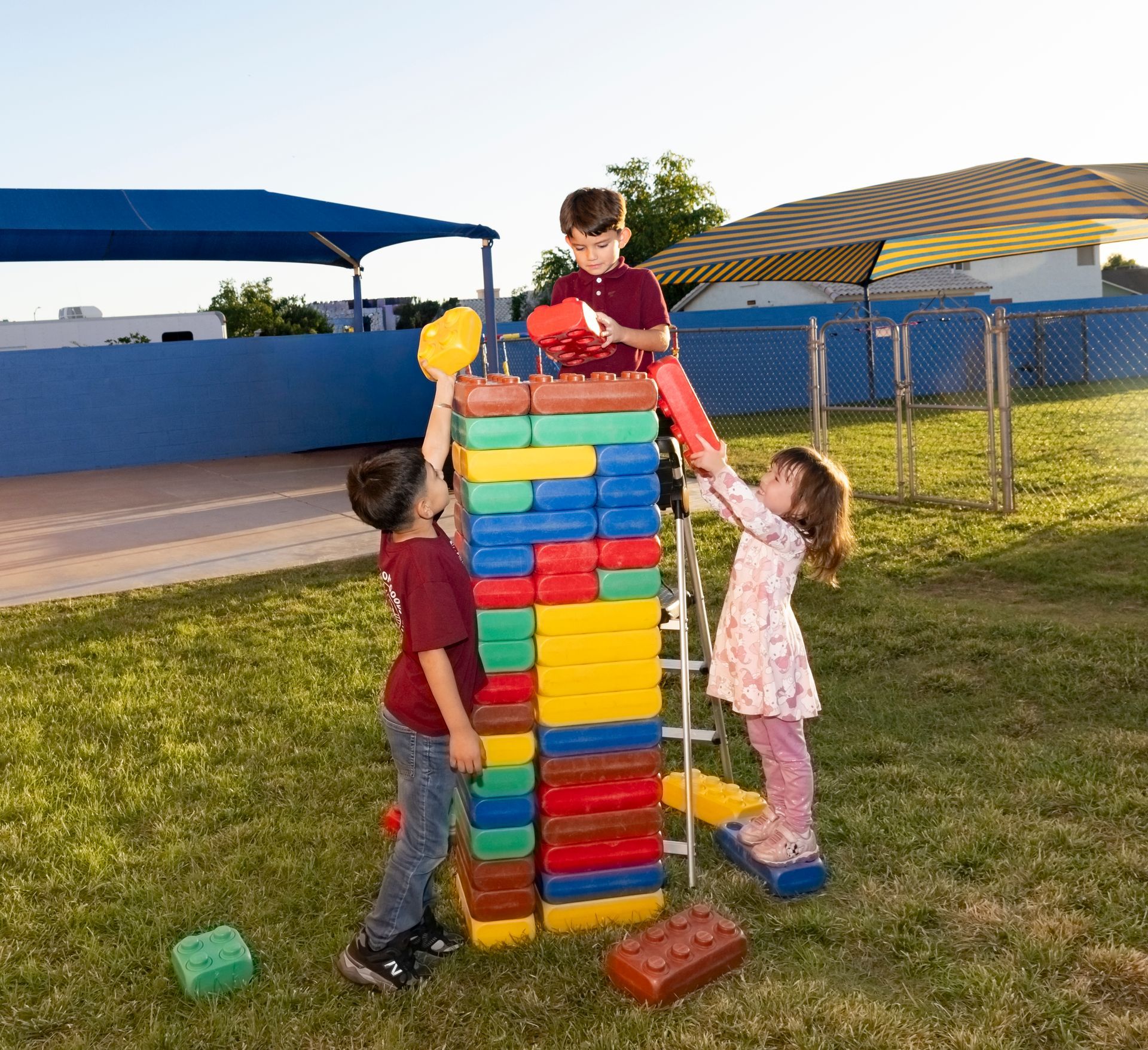 Children stacking colorful giant blocks outdoors under striped canopies