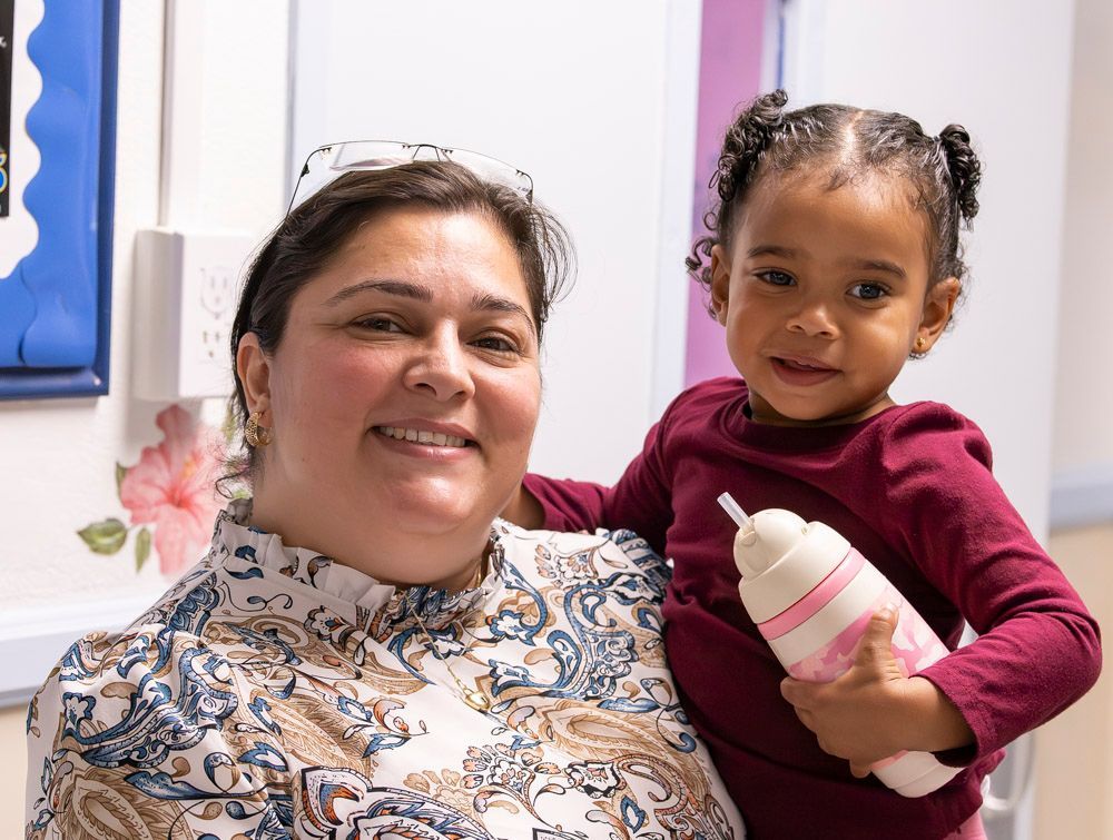 Smiling woman holding a child with a bottle in a bright indoor room