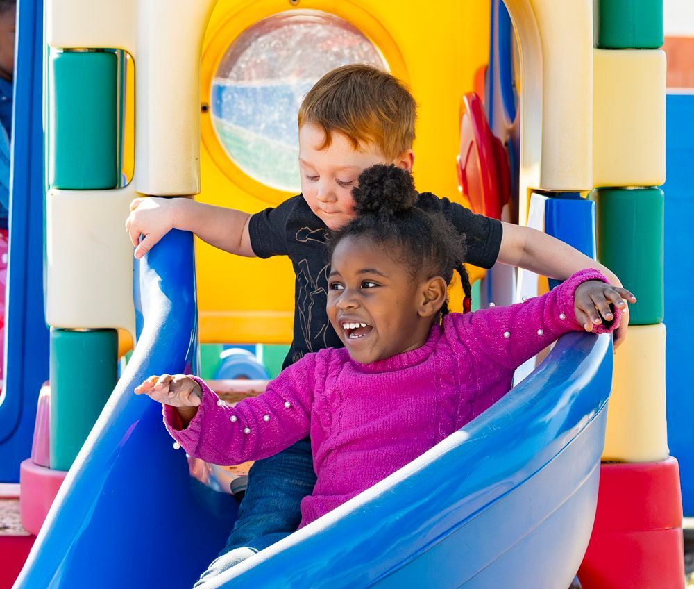 Two children sliding down a colorful playground slide, smiling and playing together.