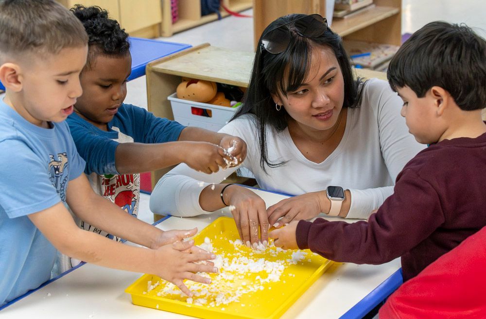Teacher and children shaping dough at a classroom table with a yellow tray
