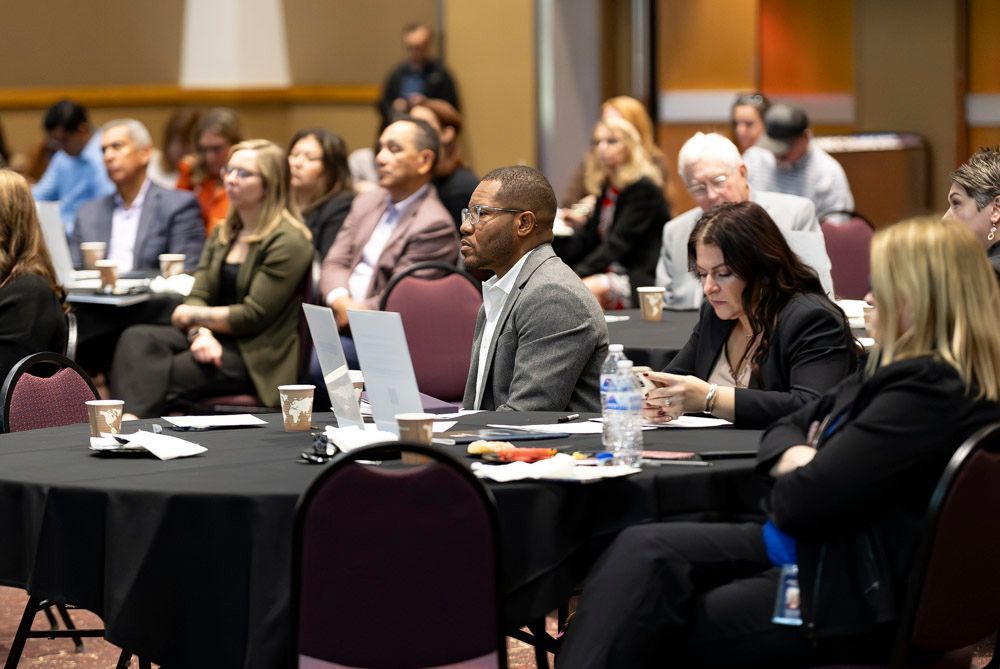 Audience seated at tables in a conference room, listening during a presentation