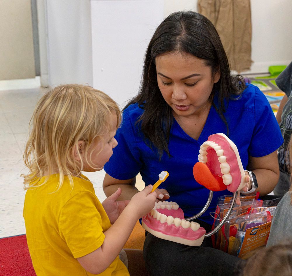 Woman showing a child how to brush a model of teeth in a classroom setting