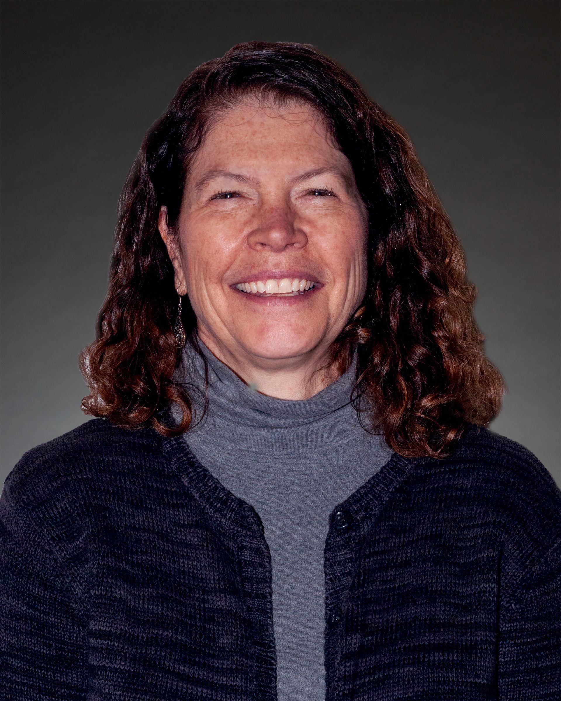 a woman with curly hair and a turtleneck is smiling for the camera .